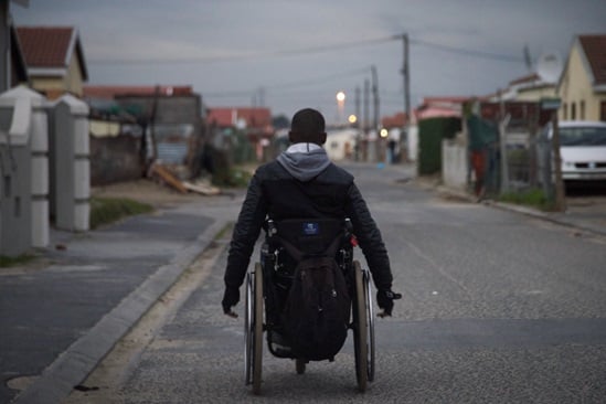 A man driving his wheelchair on a street in the evening